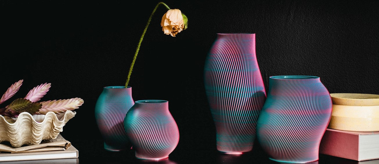 Eine Sammlung farbenfroher, gerippter Vasen in verschiedenen Größen mit einer einzelnen gelben Blume, umgeben von Dekorationsgegenständen auf einem dunklen Hintergrund.